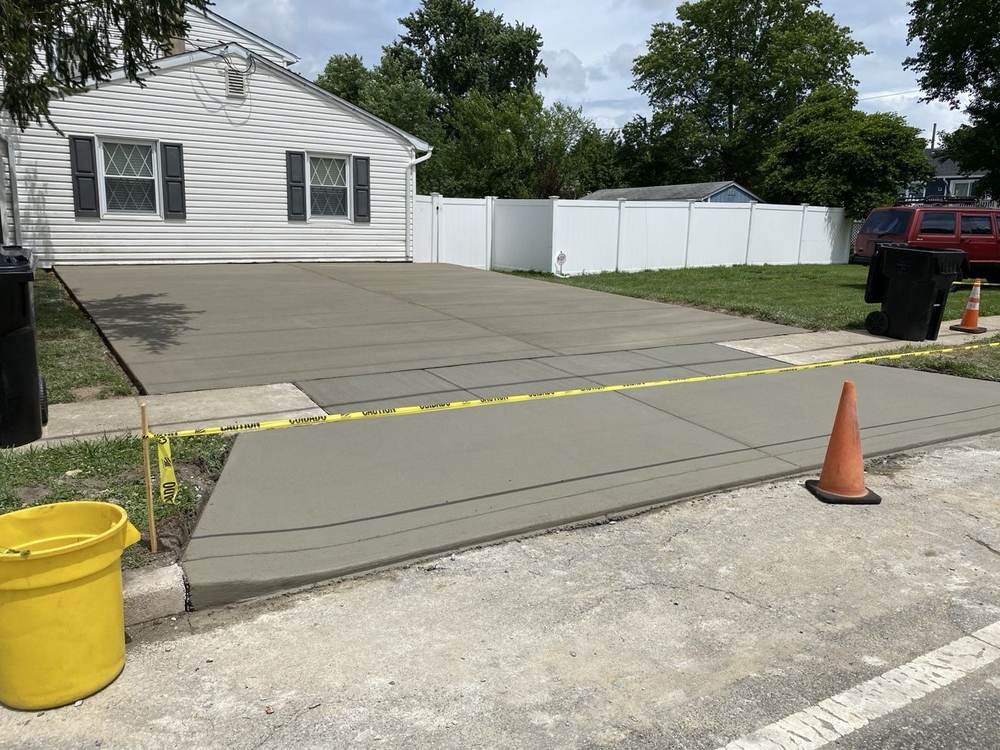 Fresh concrete driveway installed by South Jersey Construction Enterprise at a white house, curing behind caution tape